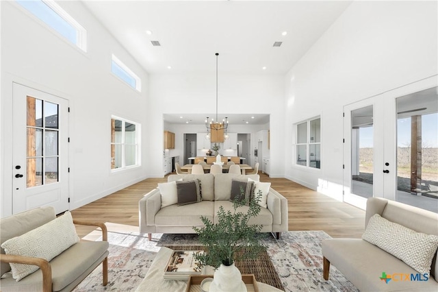 living room with a high ceiling, light wood-type flooring, a notable chandelier, and a healthy amount of sunlight