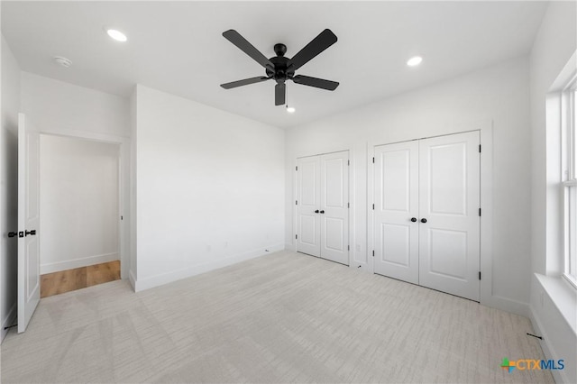 unfurnished bedroom featuring ceiling fan, multiple windows, light carpet, and two closets