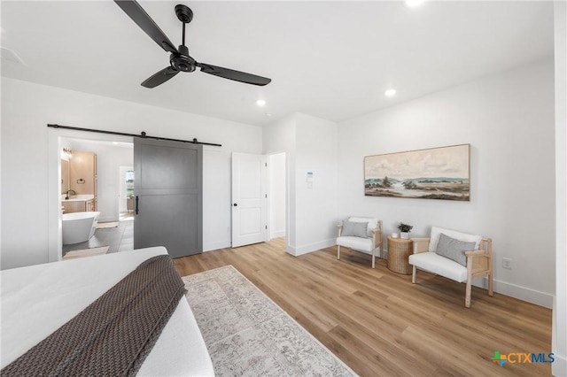 bedroom featuring wood-type flooring, a barn door, ceiling fan, and connected bathroom