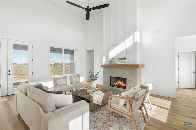 living room featuring french doors, ceiling fan, light hardwood / wood-style flooring, a fireplace, and a high ceiling