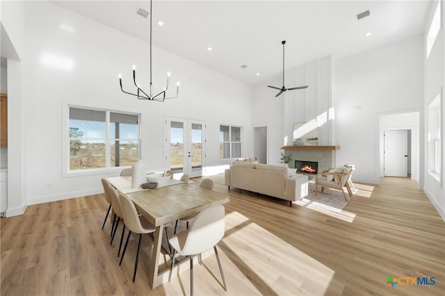 dining space featuring ceiling fan with notable chandelier, french doors, a high ceiling, and light hardwood / wood-style flooring