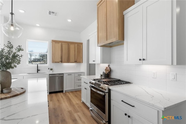 kitchen featuring sink, hanging light fixtures, appliances with stainless steel finishes, light stone counters, and white cabinetry