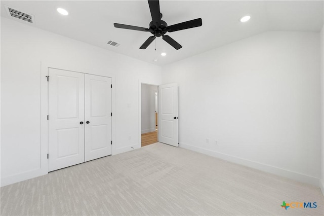 unfurnished bedroom featuring light carpet, a closet, vaulted ceiling, and ceiling fan