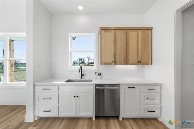 kitchen with light stone counters, stainless steel dishwasher, sink, white cabinets, and light hardwood / wood-style floors