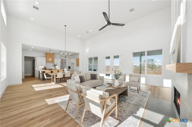 living room featuring a tile fireplace, french doors, a high ceiling, light hardwood / wood-style flooring, and ceiling fan with notable chandelier