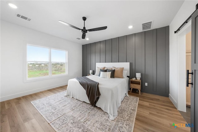 bedroom featuring a barn door, ceiling fan, and light hardwood / wood-style floors