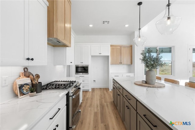 kitchen featuring light stone counters, light hardwood / wood-style floors, pendant lighting, stainless steel stove, and white cabinetry