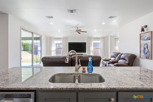 kitchen with a center island with sink, light stone counters, sink, stainless steel dishwasher, and ceiling fan