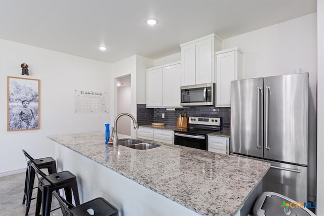 kitchen with light stone counters, sink, an island with sink, white cabinetry, and appliances with stainless steel finishes