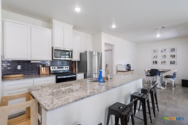 kitchen featuring white cabinetry, appliances with stainless steel finishes, backsplash, a breakfast bar area, and a kitchen island with sink