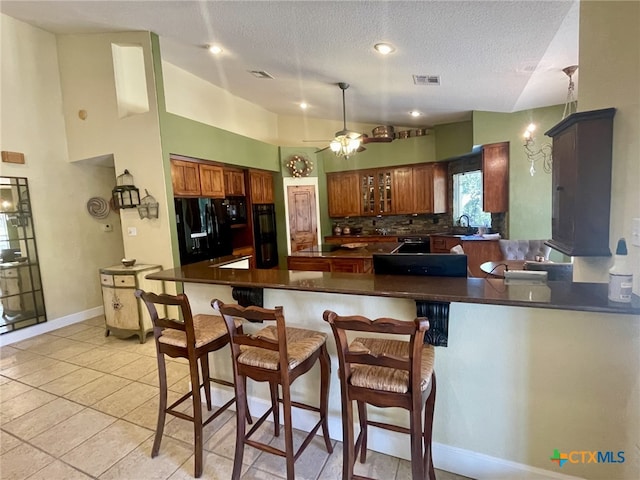 kitchen with backsplash, black fridge, light tile patterned flooring, a kitchen bar, and kitchen peninsula