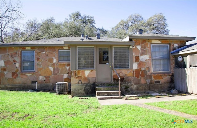 rear view of property featuring cooling unit, stone siding, and a lawn