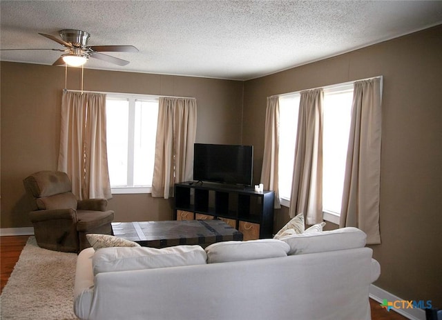 living area with plenty of natural light, dark wood-type flooring, a ceiling fan, and a textured ceiling