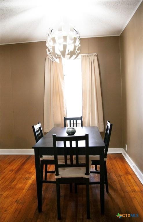 dining room with wood finished floors, baseboards, an inviting chandelier, a textured ceiling, and crown molding