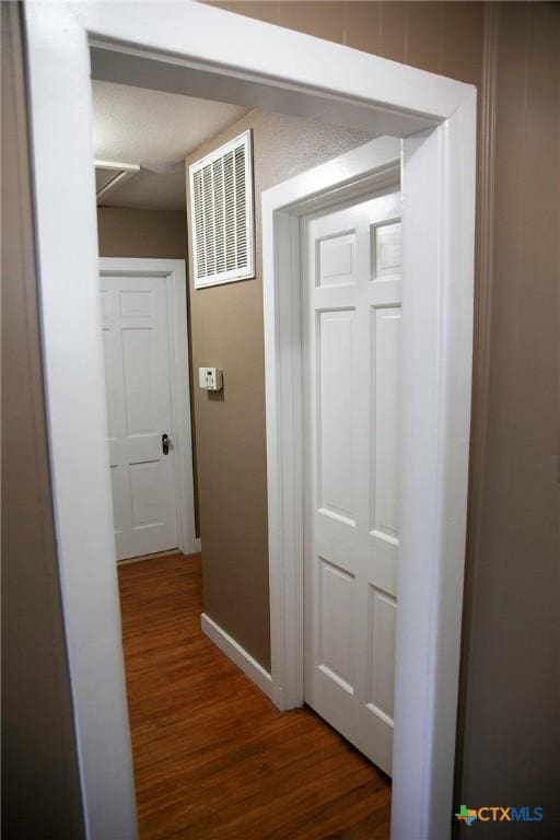 hall with visible vents, baseboards, and wood finished floors