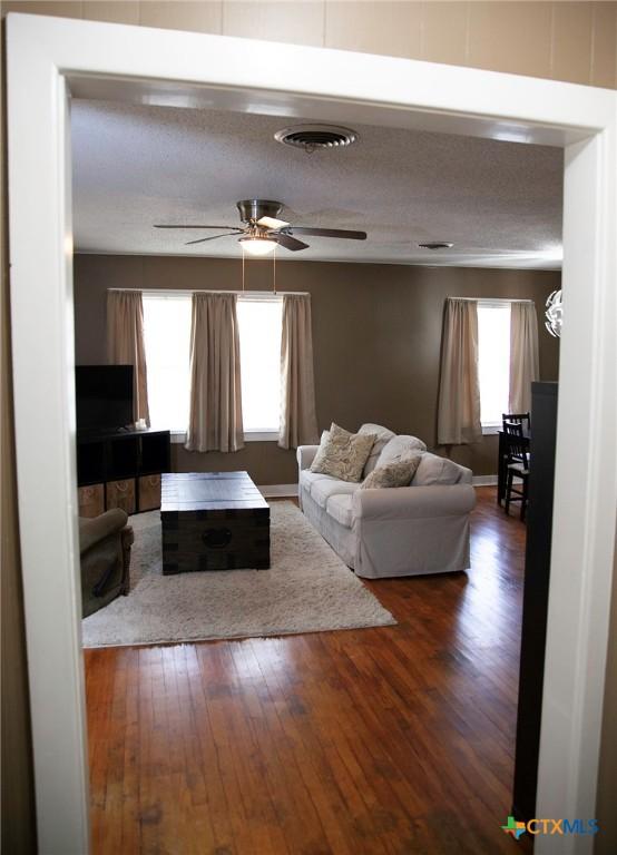 living room featuring a ceiling fan, visible vents, wood-type flooring, and a textured ceiling