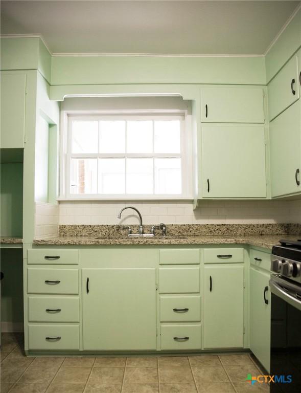 kitchen featuring a sink, tasteful backsplash, stainless steel range with gas stovetop, and green cabinets