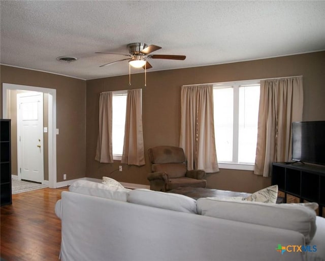 living room featuring a ceiling fan, baseboards, wood finished floors, visible vents, and a textured ceiling