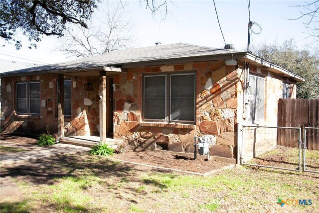 rear view of property with stone siding, roof with shingles, and fence