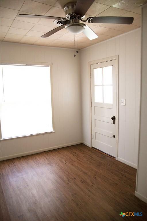 unfurnished room with a ceiling fan, plenty of natural light, wood finished floors, and baseboards