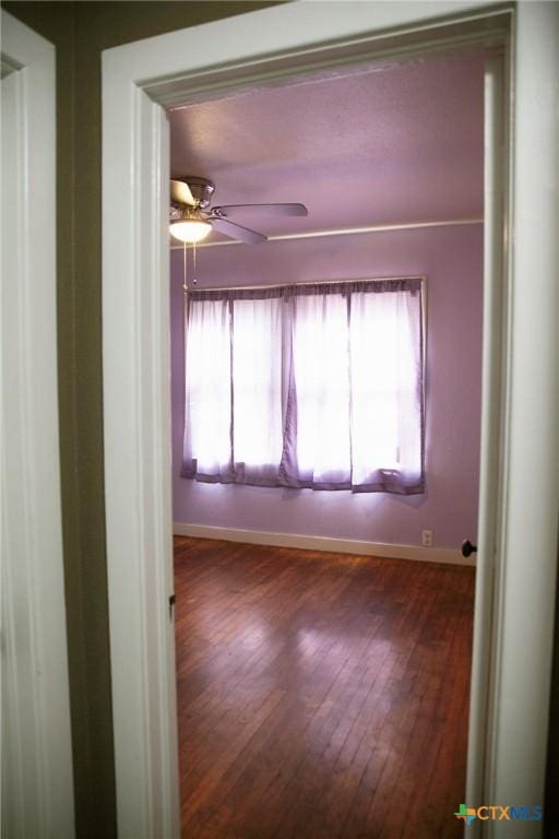 unfurnished room featuring a wealth of natural light, dark wood-style floors, baseboards, and ceiling fan