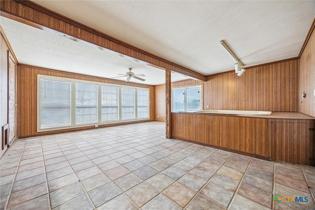 kitchen with a textured ceiling, wooden walls, brown cabinetry, light tile patterned floors, and ceiling fan