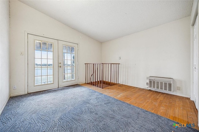 empty room featuring wood finished floors, vaulted ceiling, french doors, a wall mounted air conditioner, and a textured ceiling