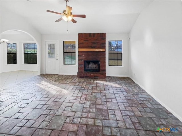 unfurnished living room with vaulted ceiling, a brick fireplace, ceiling fan, and plenty of natural light