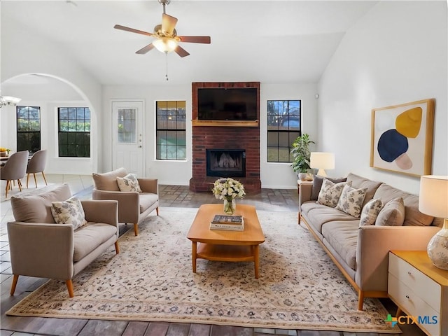 living room with ceiling fan, lofted ceiling, and a brick fireplace