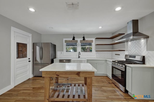 kitchen featuring wall chimney range hood, sink, light hardwood / wood-style flooring, appliances with stainless steel finishes, and white cabinetry