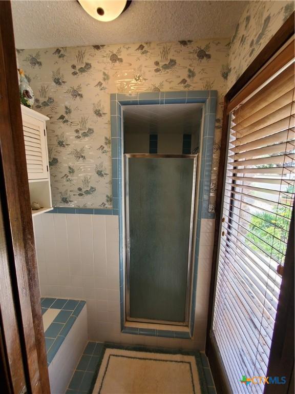 313 N Church, Goliad, TX 77963 - bathroom featuring wallpapered walls, a stall shower, a textured ceiling, wainscoting, and tile walls