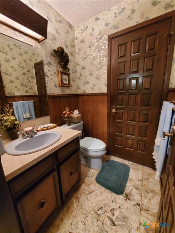 313 N Church, Goliad, TX 77963 - bathroom with a wainscoted wall, vanity, wallpapered walls, toilet, and a textured ceiling