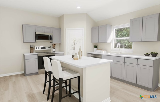 kitchen featuring light wood-type flooring, gray cabinetry, stainless steel appliances, a kitchen island, and lofted ceiling