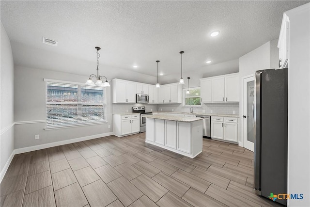 3305 Crystal Ann Dr, Temple, TX 76502 - kitchen with stainless steel appliances, white cabinets, a chandelier, a kitchen island, and a textured ceiling