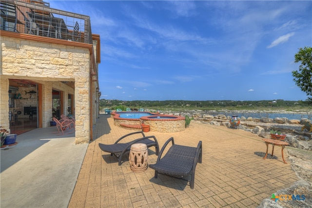 view of patio with a water view and an in ground hot tub