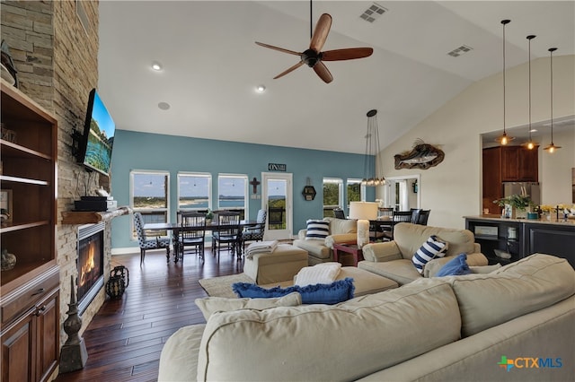 living room with a fireplace, ceiling fan with notable chandelier, dark wood-type flooring, and high vaulted ceiling