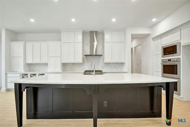 kitchen with light wood-type flooring, built in microwave, a spacious island, wall chimney range hood, and white cabinetry