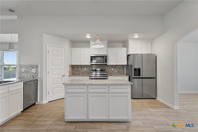 kitchen featuring appliances with stainless steel finishes, arched walkways, tasteful backsplash, white cabinetry, and light wood-style floors