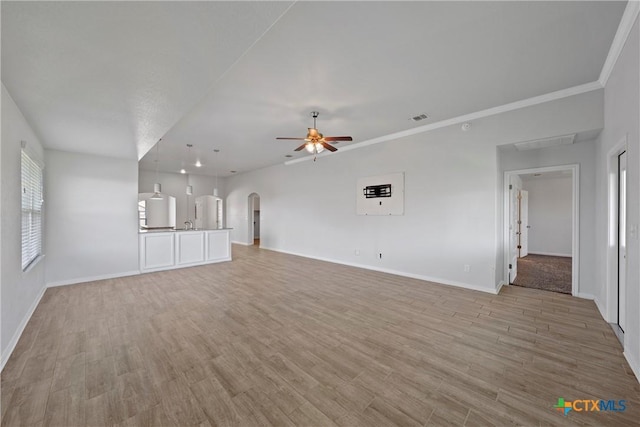 unfurnished living room featuring a ceiling fan, arched walkways, baseboards, and light wood-type flooring