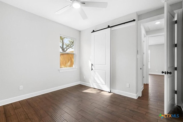 unfurnished bedroom with ceiling fan, a barn door, and dark hardwood / wood-style floors