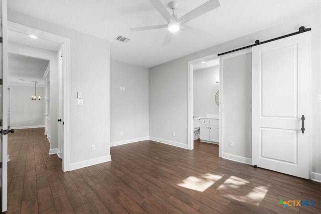 unfurnished bedroom featuring ensuite bathroom, ceiling fan with notable chandelier, dark wood-type flooring, and a barn door