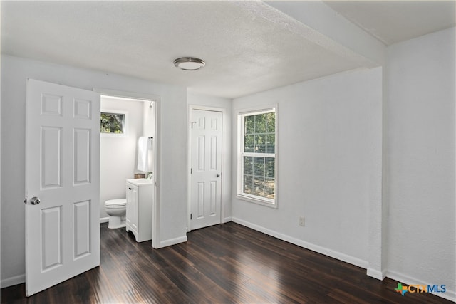 unfurnished bedroom featuring ensuite bath, dark hardwood / wood-style flooring, and a textured ceiling