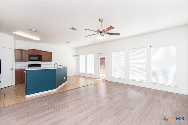 1217 Roanoke Dr, Temple, TX 76504 - kitchen with black microwave, light countertops, a ceiling fan, decorative backsplash, and light wood-style floors