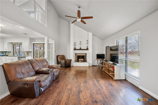 living room with dark wood-type flooring, a large fireplace, and ceiling fan