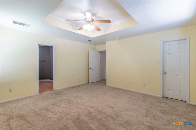 unfurnished bedroom with a walk in closet, light carpet, ceiling fan, and a raised ceiling