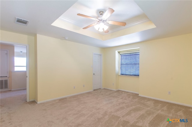 empty room with ornamental molding, light colored carpet, ceiling fan, and a raised ceiling