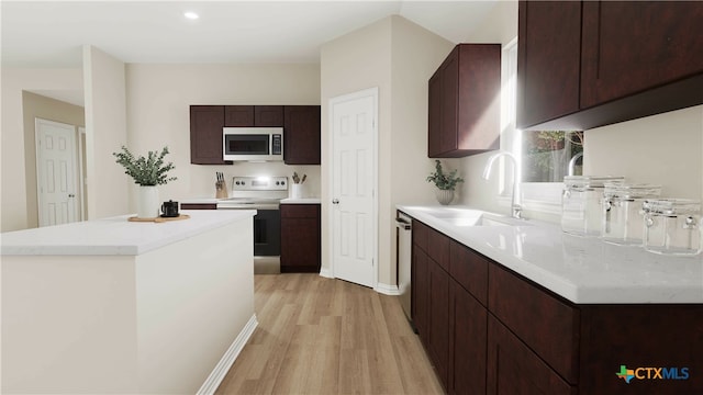 kitchen featuring stainless steel appliances, dark brown cabinetry, sink, a kitchen island, and light wood-type flooring