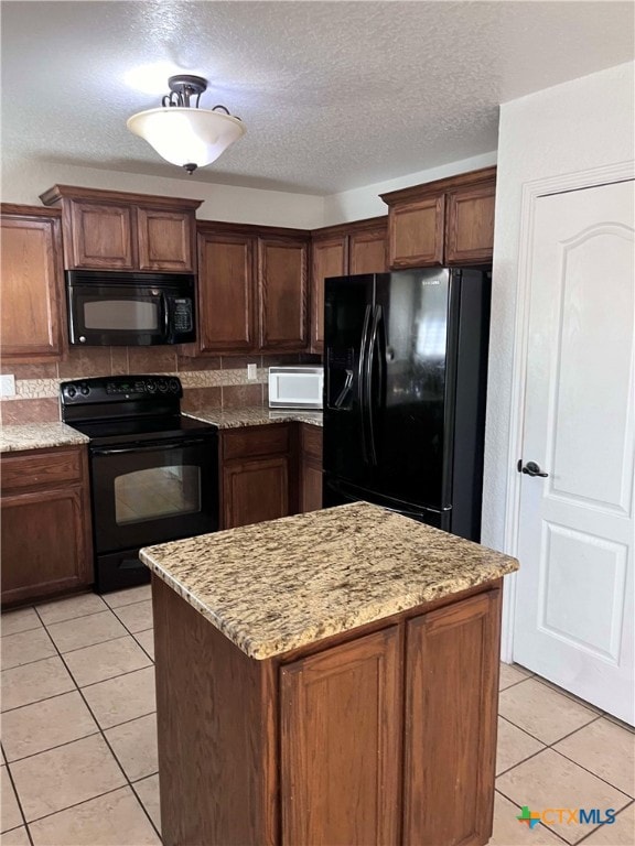 kitchen featuring black appliances, light stone countertops, a textured ceiling, light tile patterned floors, and a kitchen island