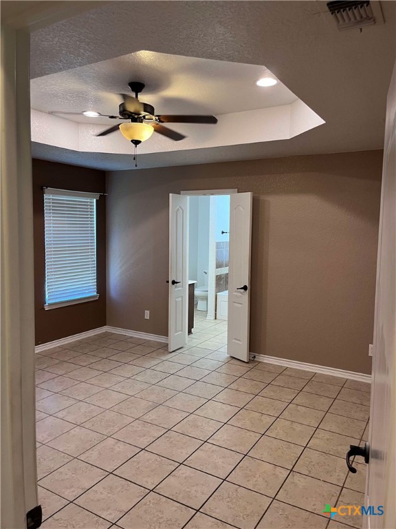 tiled spare room with a textured ceiling, a tray ceiling, and ceiling fan