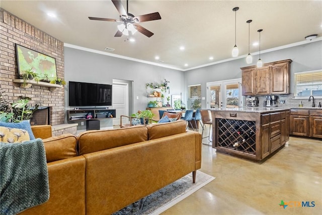 living room with ceiling fan, crown molding, sink, and a brick fireplace